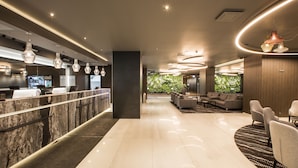 A modern hotel lobby with a reception desk, seating area, and a view of greenery.