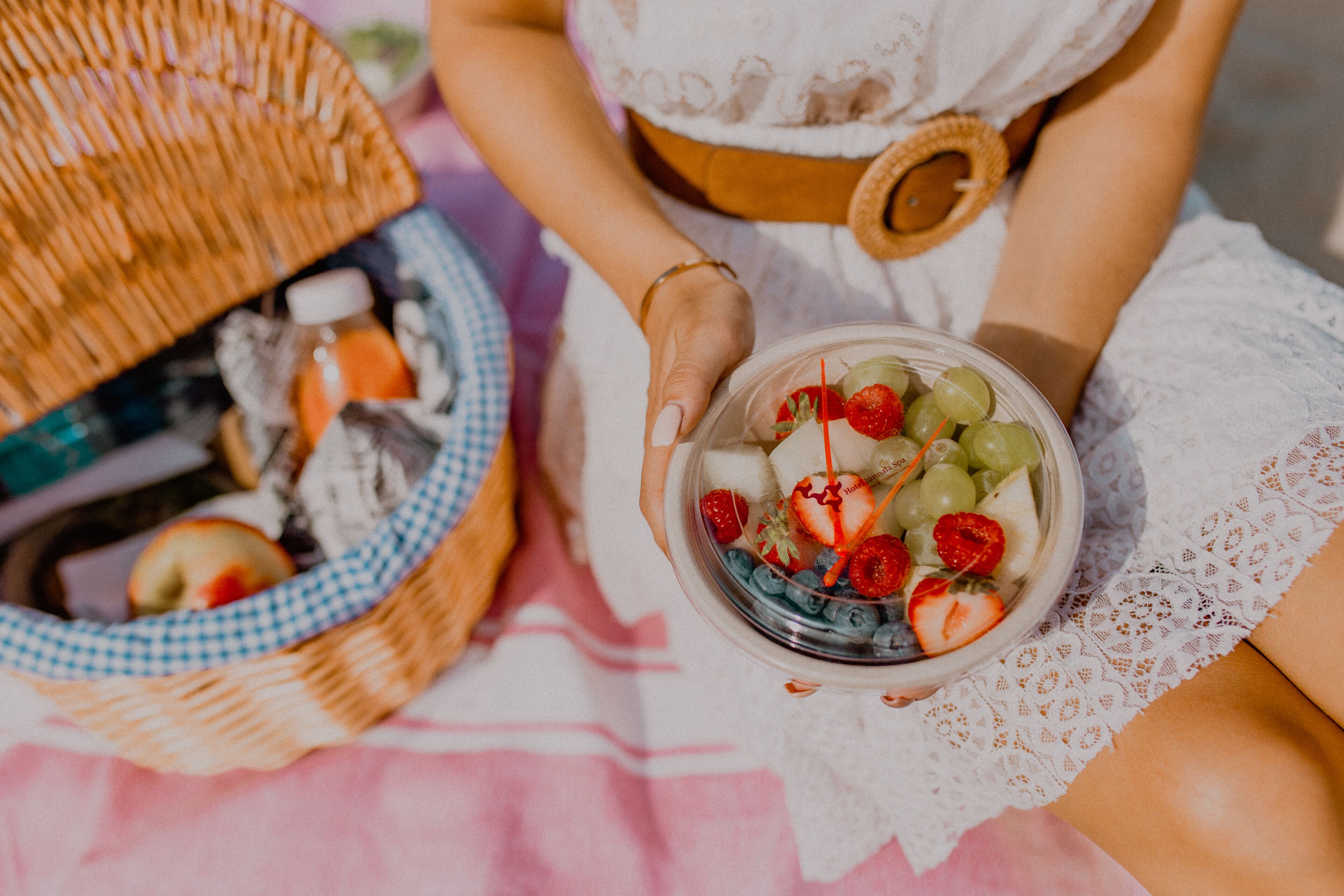 A person holding a bowl of fruit salad with strawberries, grapes, and blueberries.