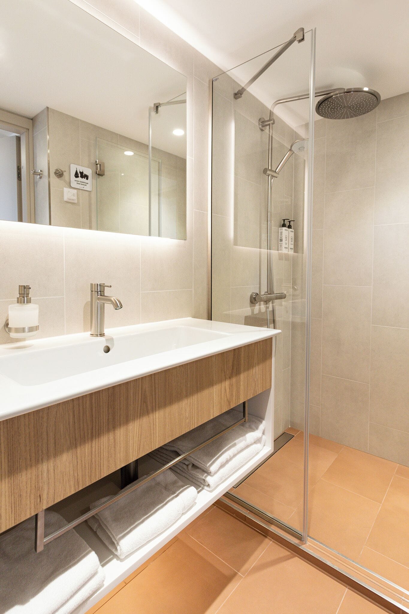 Une salle de bain moderne avec une douche à parois de verre, un grand lavabo avec un miroir et des serviettes soigneusement pliées.