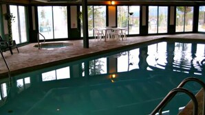 Una piscina interior amb parets de vidre transparent, un paviment de rajoles i algunes cadires i taules al voltant de la piscina.