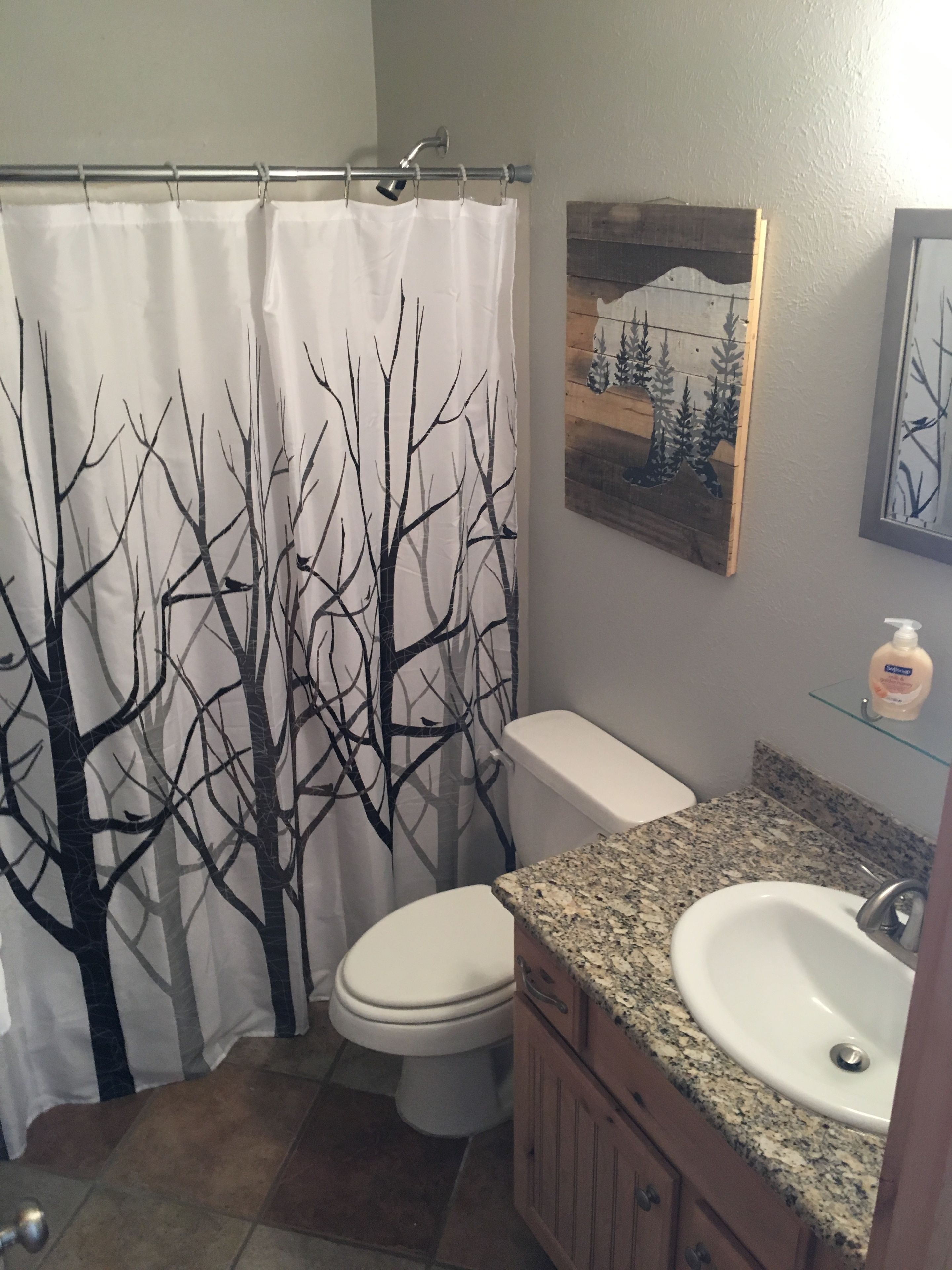 A bathroom with a tree-patterned shower curtain, a toilet, a sink, and a wooden cabinet.