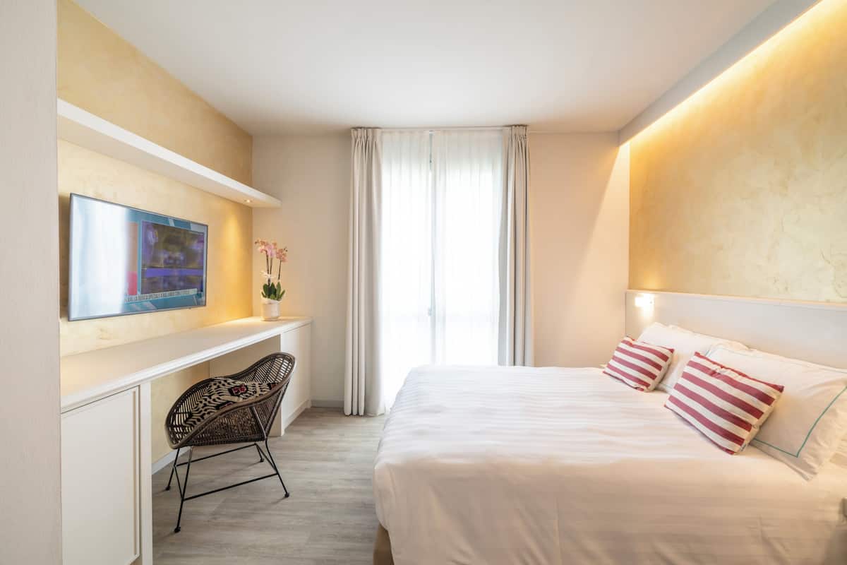 A hotel room with a bed, a desk, a chair, a TV, and a window with curtains.