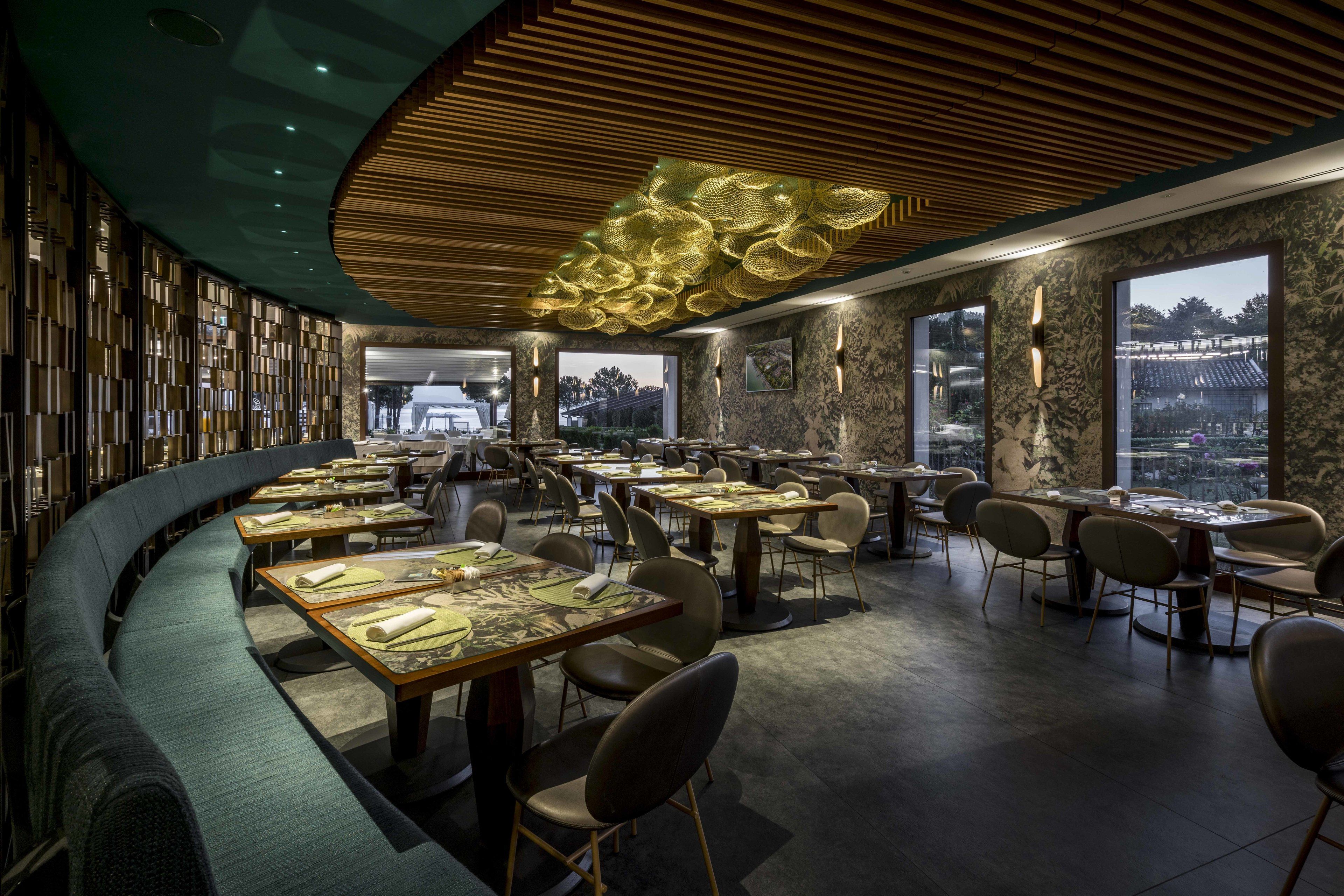 A modern restaurant with a curved seating area, wooden ceiling, and large windows offering views of the outside.