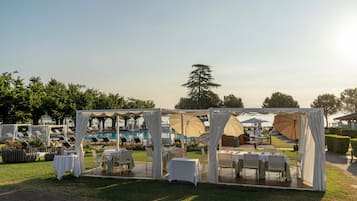 Patio esterno con tavoli, sedie, piscina e ombrelloni.