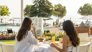 Twee personen dineren aan een tafel met uitzicht op een zwembad, met terraszitplaatsen en een buffet.