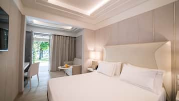 Habitación de hotel con una cama grande, un escritorio, una silla, una mesita con un teléfono y una lámpara, y un televisor montado en la pared.