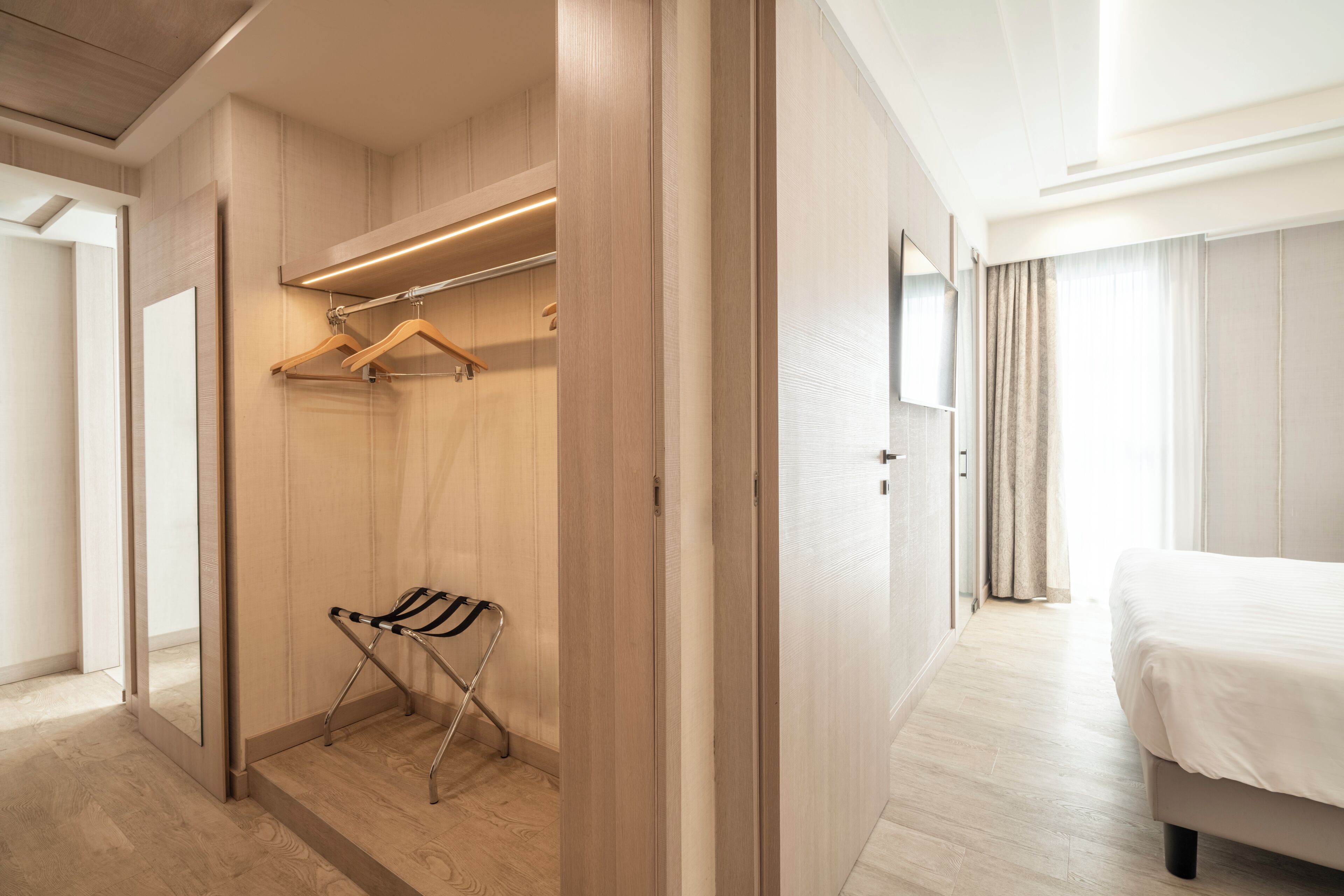 Een hotelkamer met een houten garderobe, een kledingroede, een stoel en een bed.