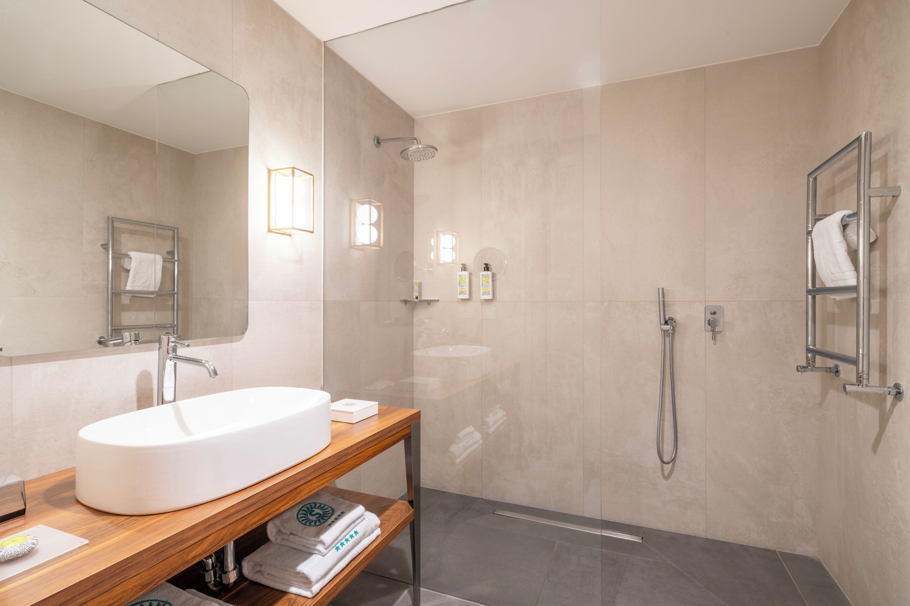 A modern bathroom with a large sink, mirror, shower, and towel racks.
