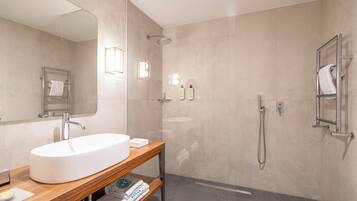 A modern bathroom with a large sink, mirror, shower, and towel racks.