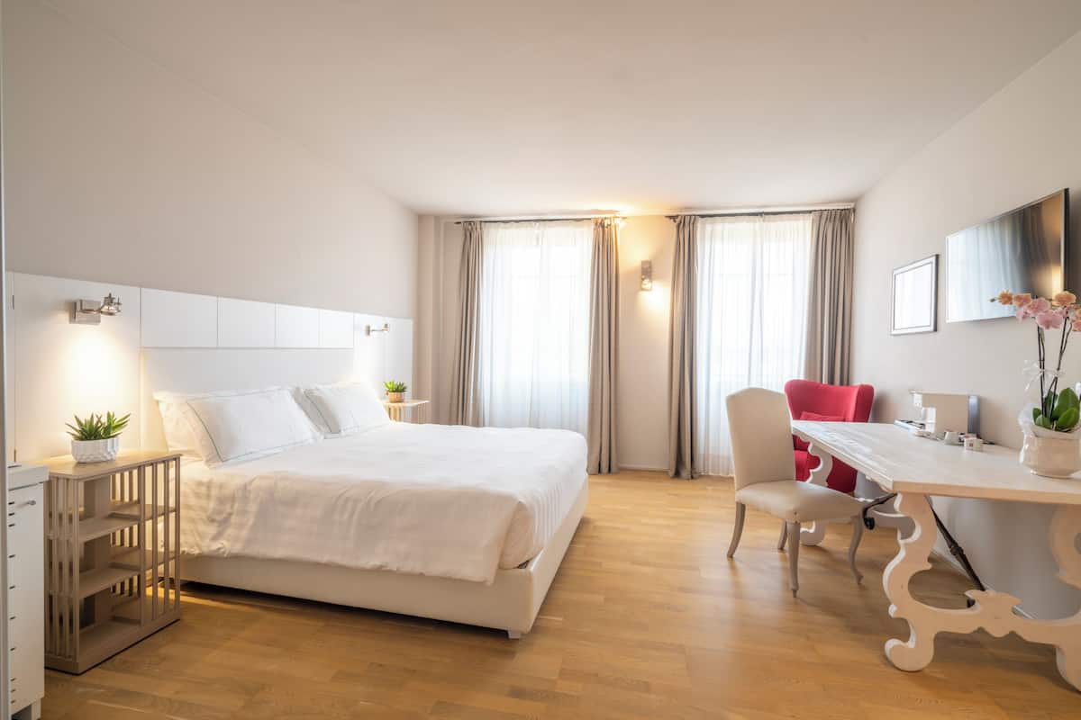 A hotel room with a bed, a desk, a chair, a TV, and a plant.