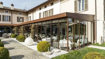 Un ristorante con posti a sedere all'aperto, pareti in vetro e un giardino curato con siepi ordinate e una grande scultura sferica.