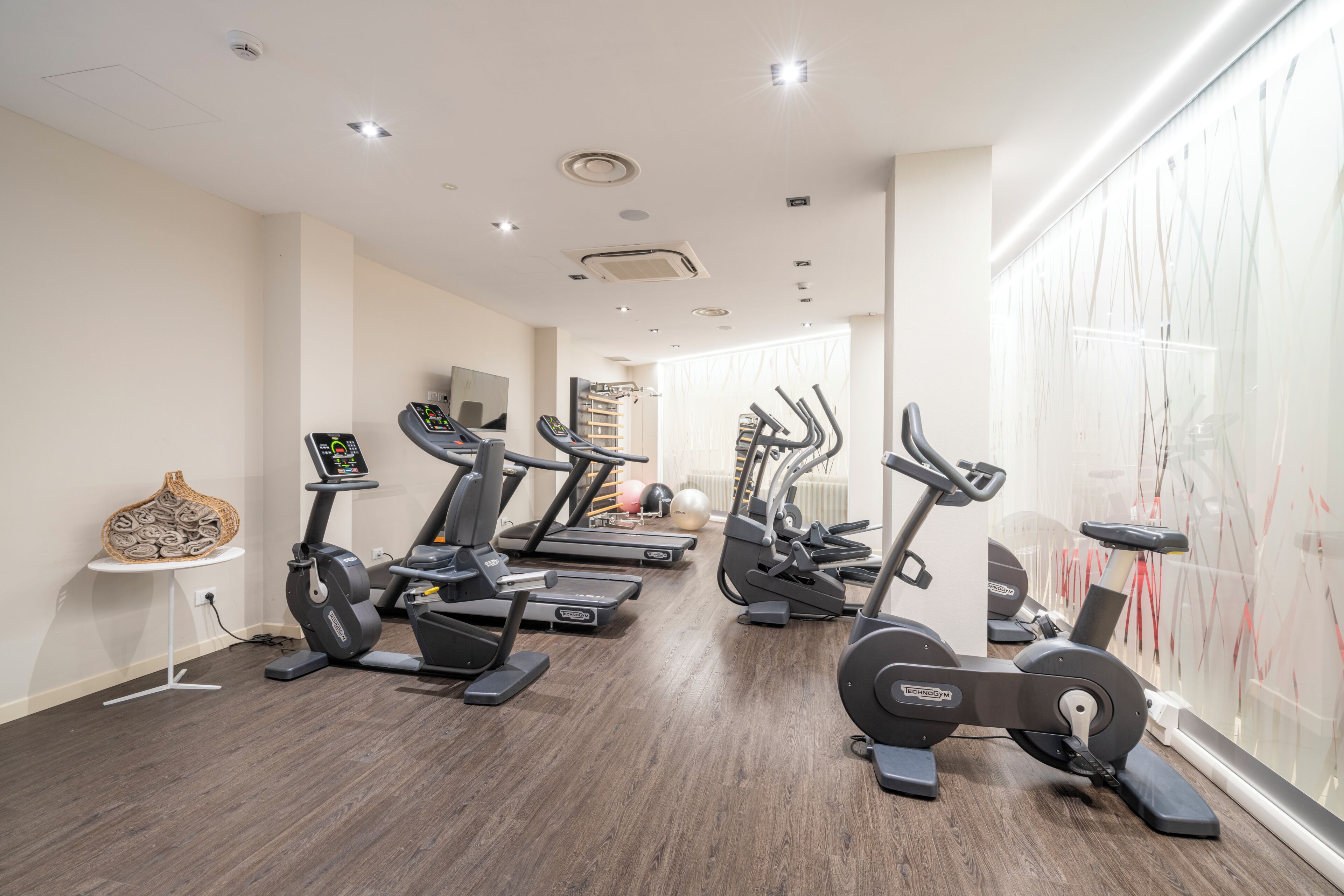 Une salle de sport équipée de matériel d’exercice, une petite table ornée d’un objet décoratif et un mur décoré d’œuvres d’art abstraites.