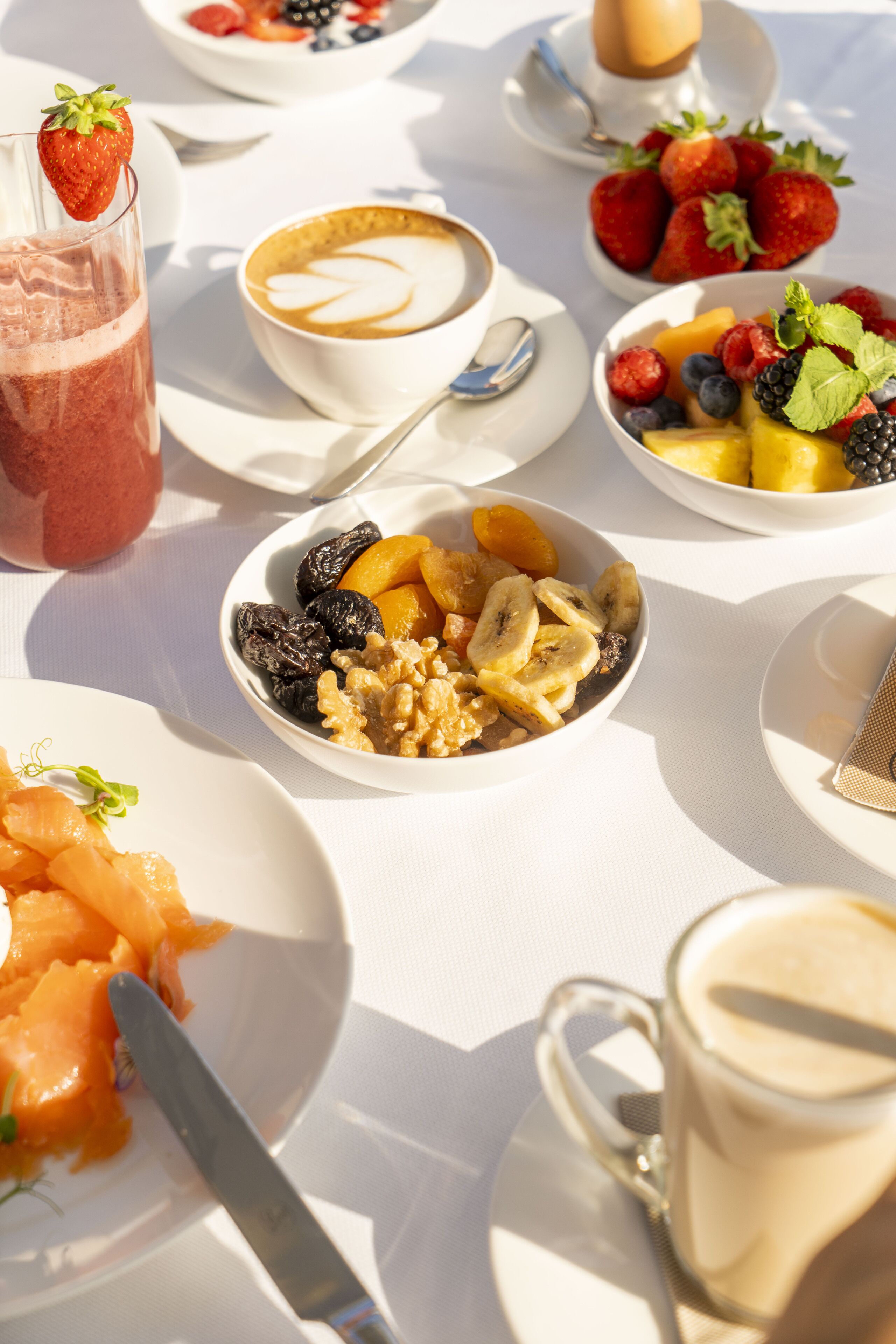 A breakfast setting with various dishes including fruits, a smoothie, and coffee.