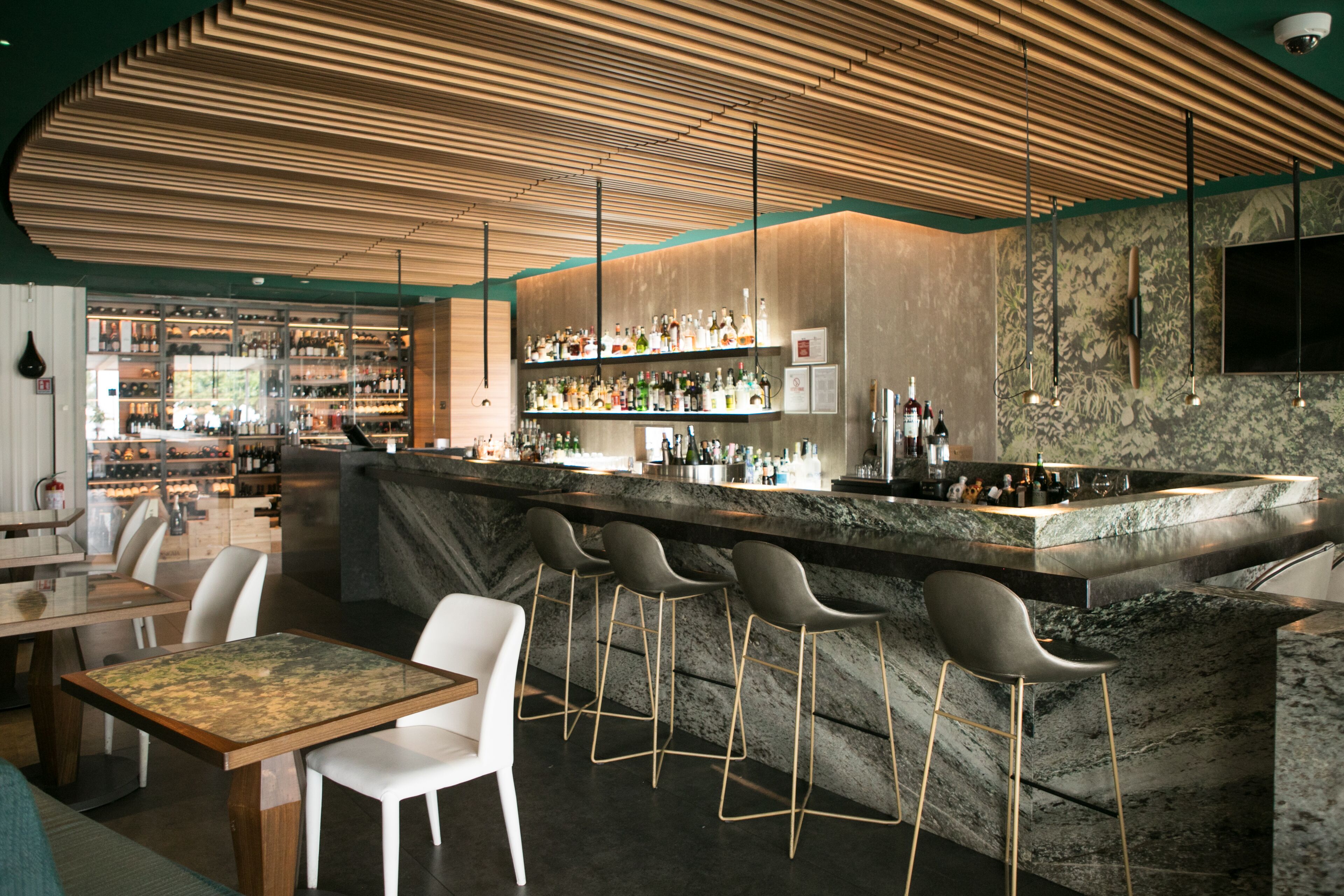 A modern bar area with a marble countertop, bar stools, and a variety of bottles.