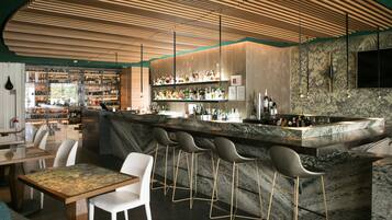 A modern bar area with a marble countertop, bar stools, and a variety of bottles.