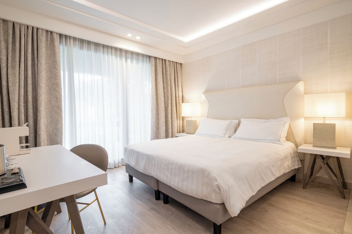 A hotel room with a bed, bedside tables, a desk, and a chair.