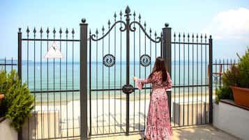 Una mujer de pie frente a una entrada con puerta de rejas, con vista al mar.