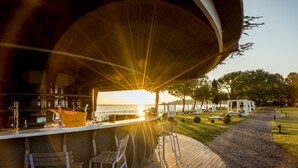 Een bar met uitzicht op een zonsondergang boven het water, buitenterras en een pad van bakstenen.