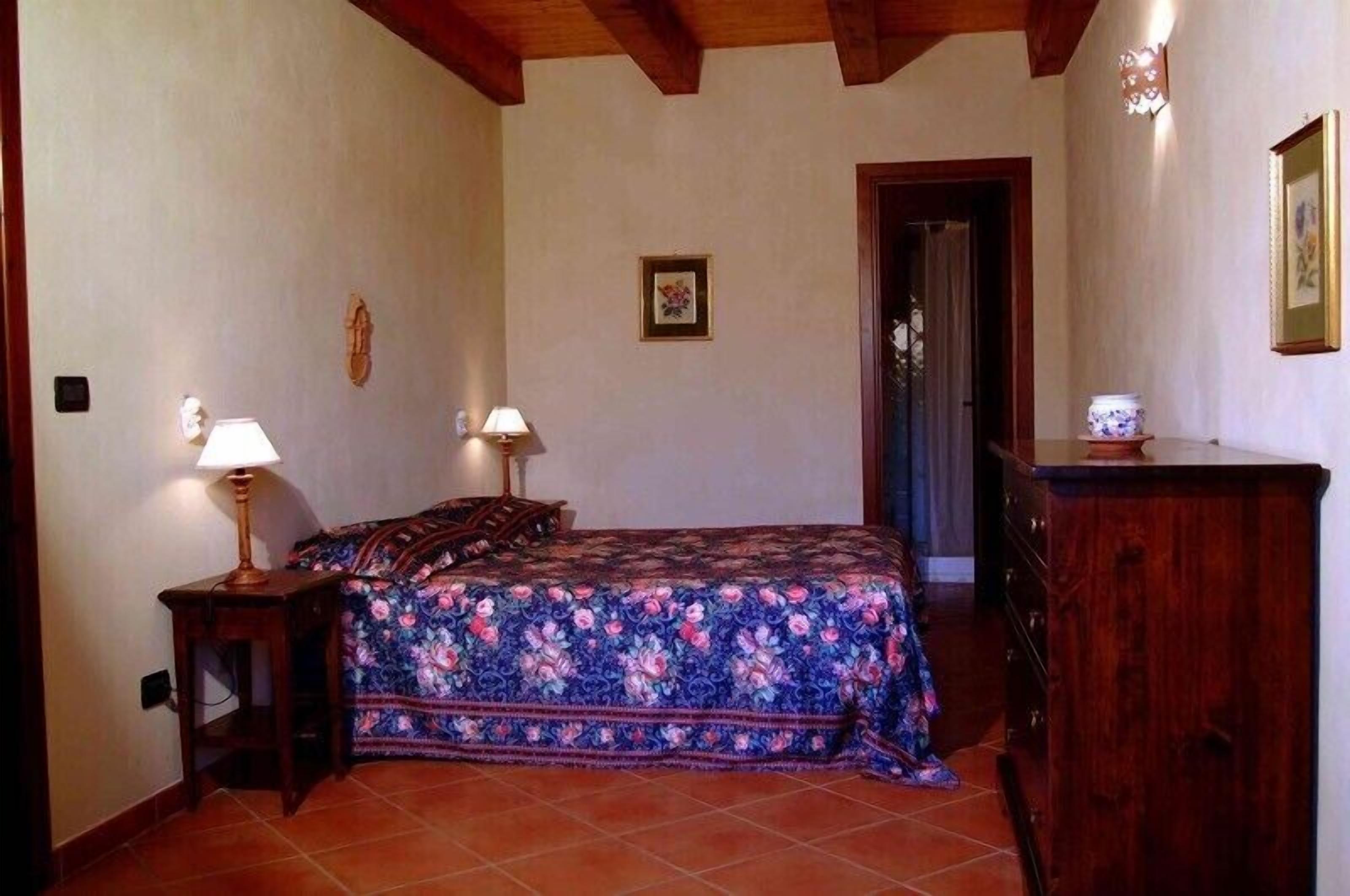 Una camera da letto con un letto, due comodini con lampade, una cassettiera e una porta che dà su un'altra stanza.