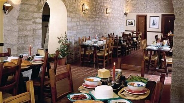 Un interior con arcos de piedra, mesas y sillas de madera, que evoca un comedor rústico.