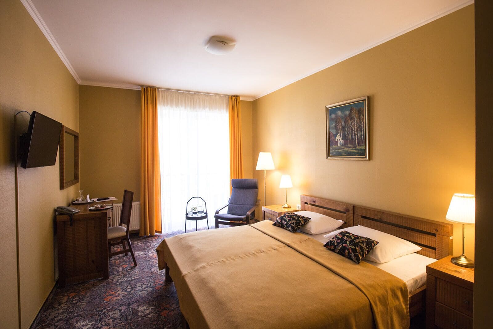 Une chambre d’hôtel comprenant un lit, deux tables de chevet avec des lampes, une chaise, un bureau avec un téléphone, une petite table avec un verre et un tableau accroché au mur.