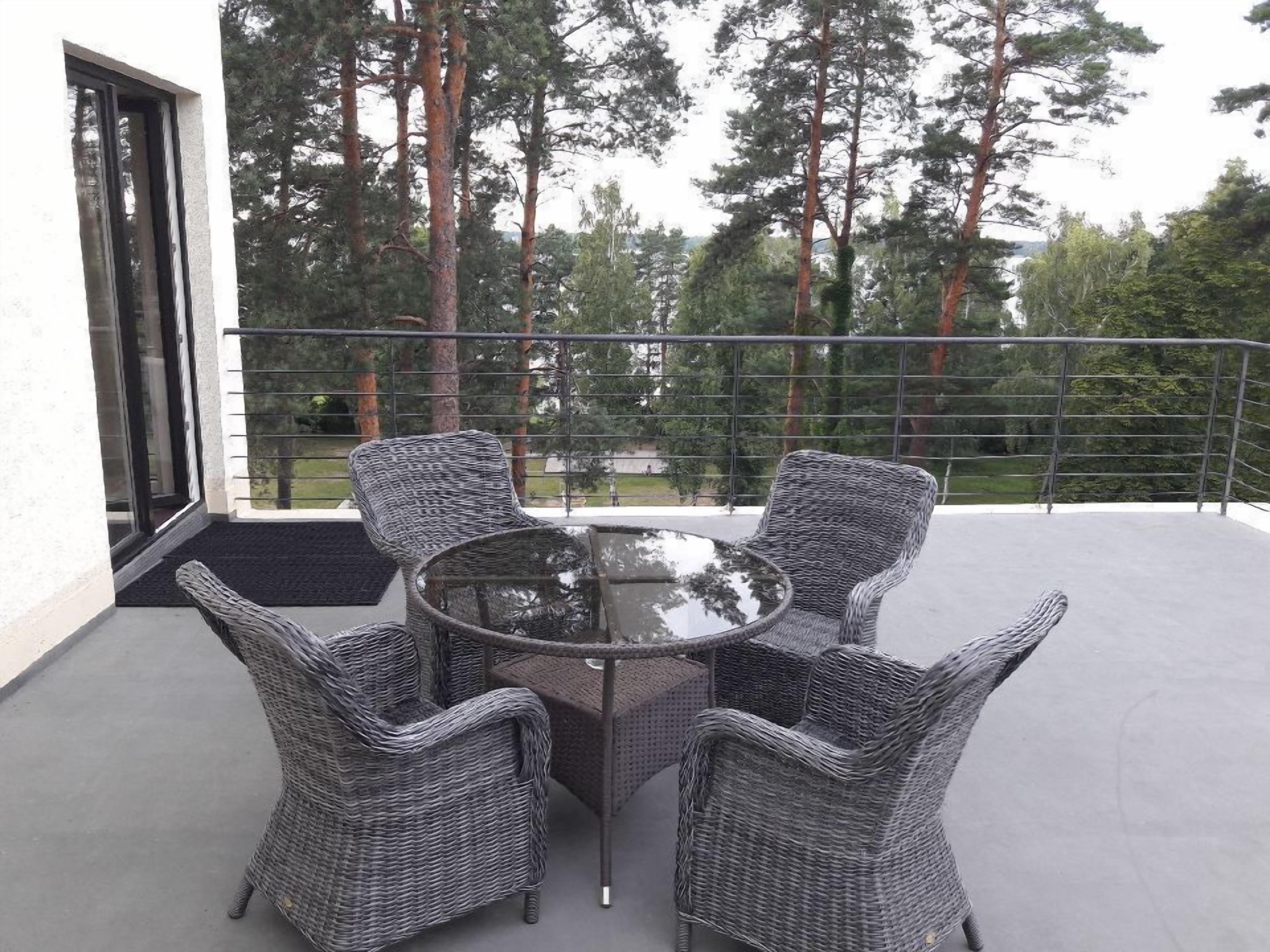 En balkon med fletmøbler og et glastæppe, med udsigt over et skovområde.