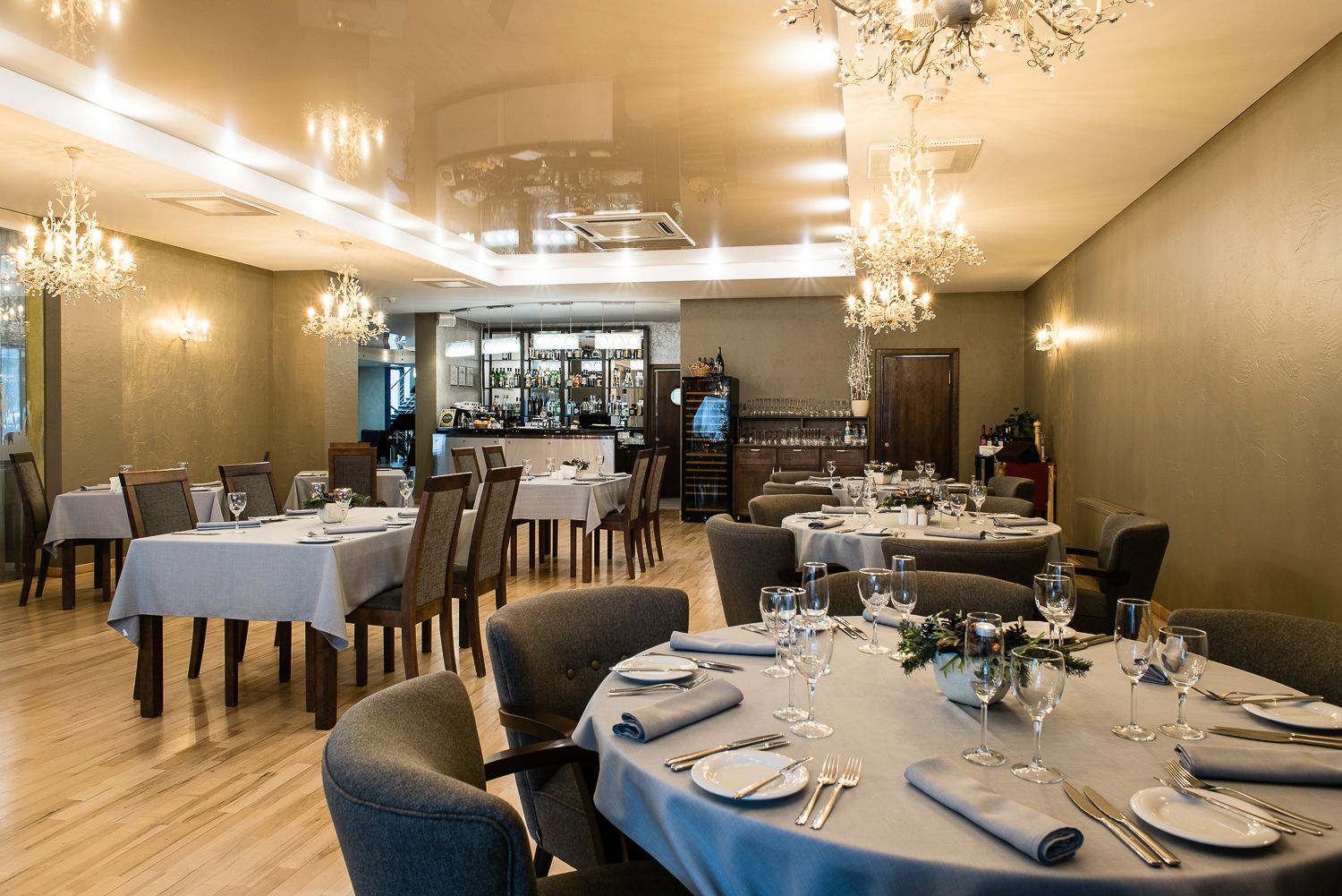 Een restaurant met ronde tafels klaar voor het dineren, een bar op de achtergrond en kroonluchters aan het plafond.