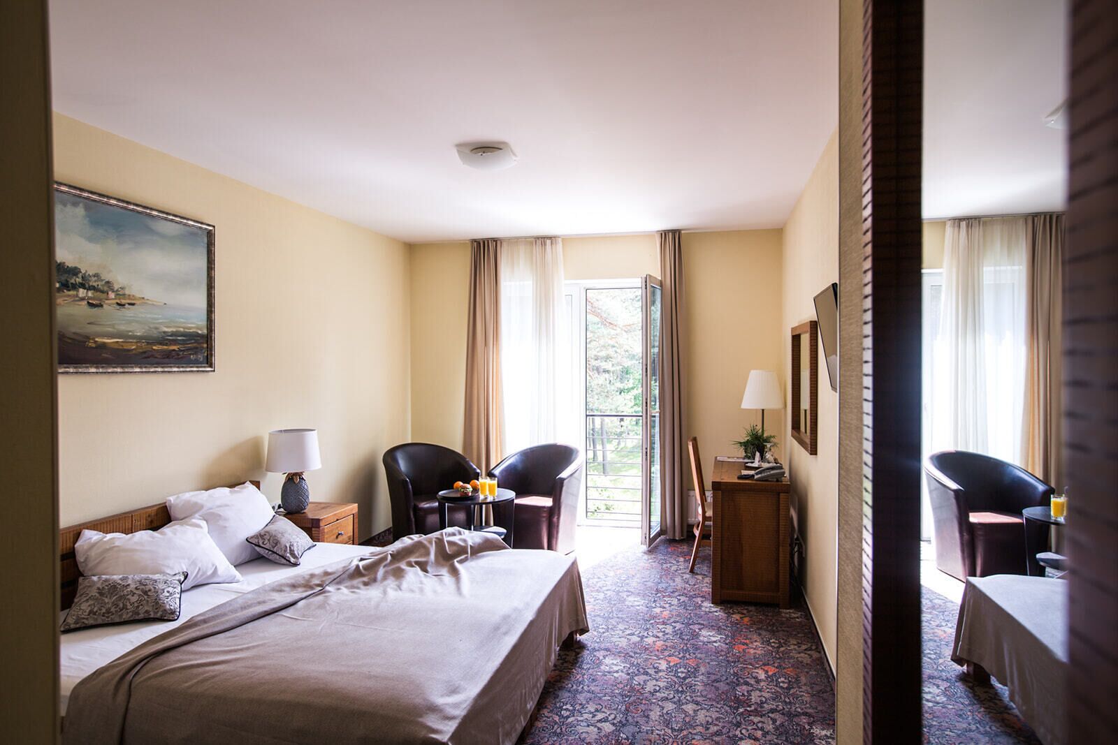 Ett hotellrum med en säng, två stolar, ett skrivbord, en tavla och utsikt över omgivningarna.