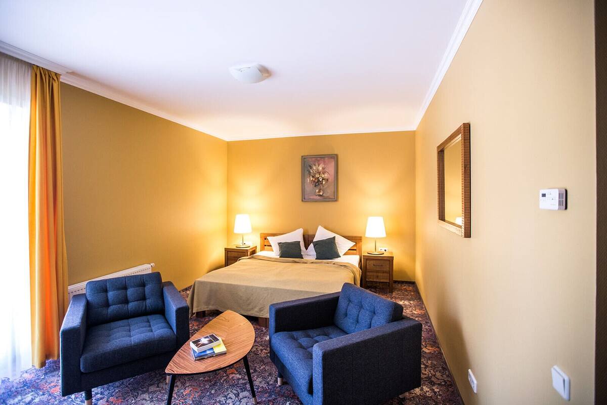 A hotel room with a bed, two armchairs, a small round table, and two bedside lamps.