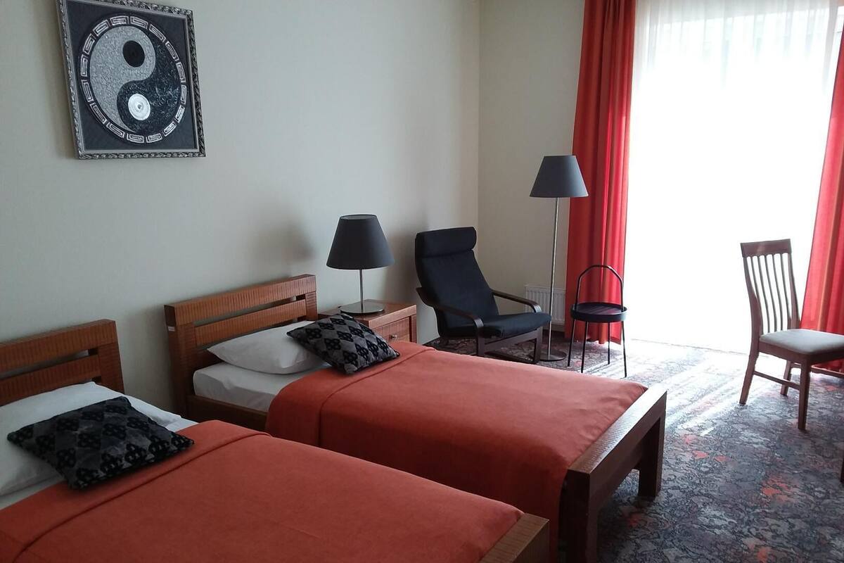 A hotel room with two beds, a desk, a chair, a lamp, and a large yin-yang symbol on the wall.
