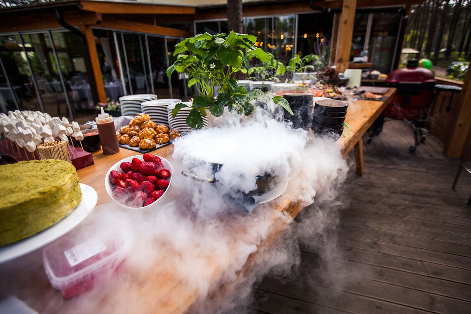 A buffet table with various food items, including a cake, strawberries, and a pot emitting steam.