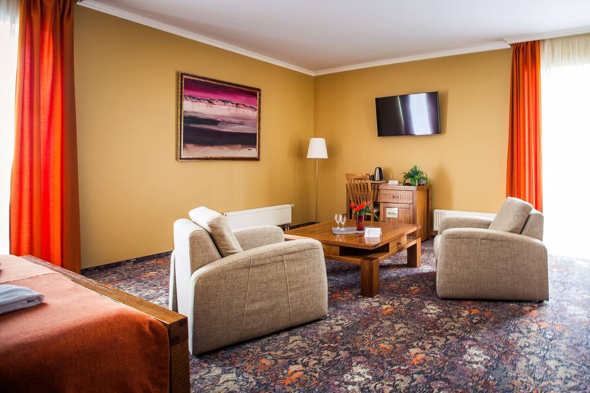 A hotel room with a sofa, armchair, and a table with a lamp and decorative items.