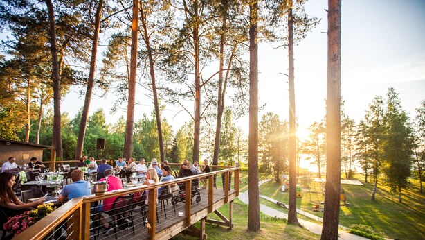 An outdoor dining area with tables and chairs, surrounded by tall trees and a grassy area. - Hotel Baltvilla (Garkalnes novads)