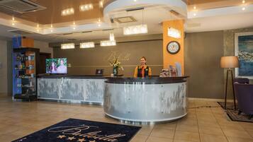 A hotel reception area with a curved reception desk, a clock on the wall, and a television screen displaying a program.