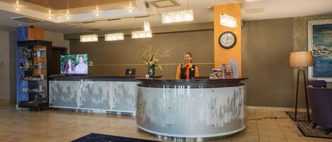 A hotel reception area with a curved reception desk, a clock on the wall, and a television screen displaying a program.