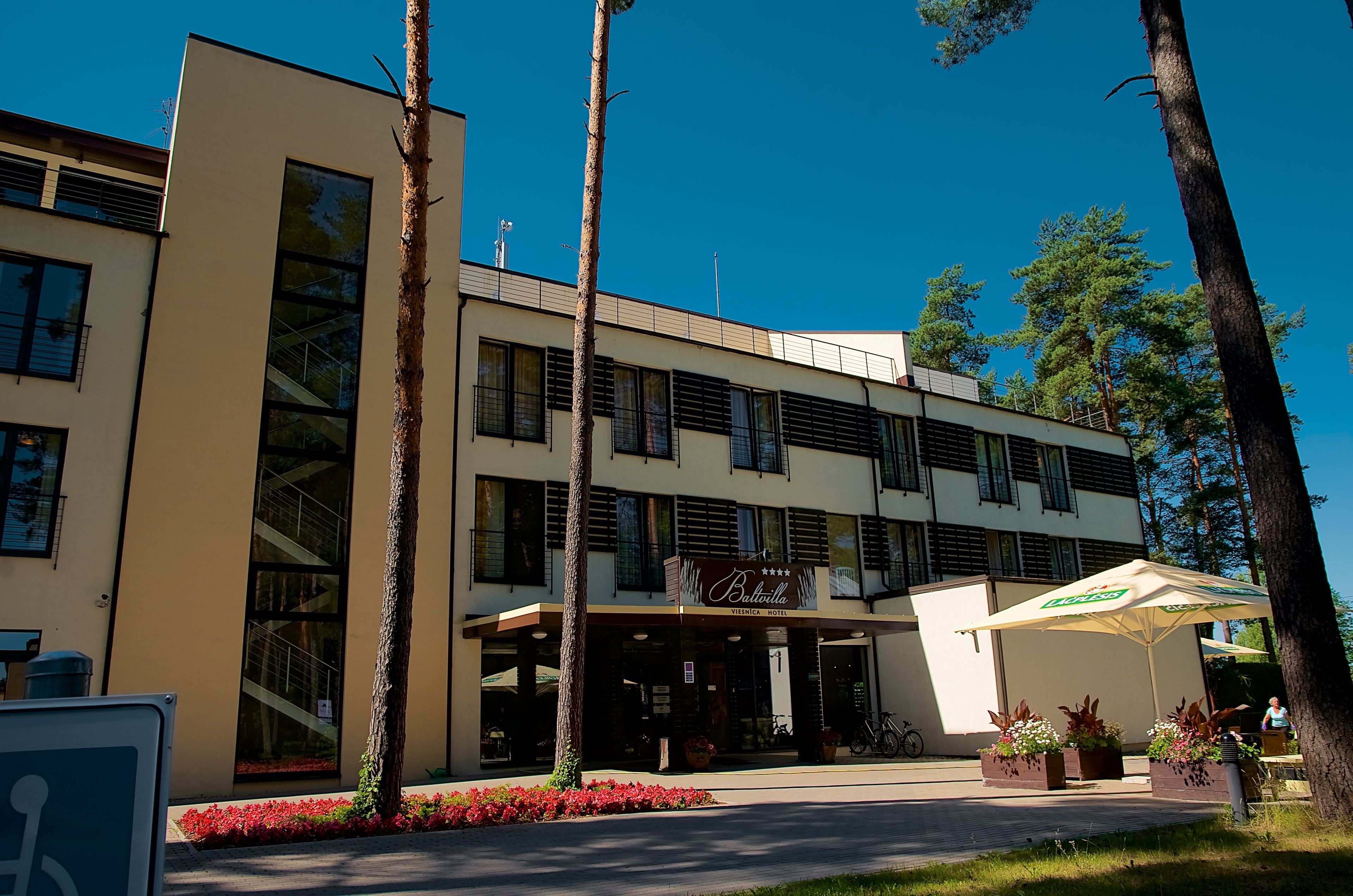 A hotel with a modern facade, large windows, and a covered outdoor seating area with plants.