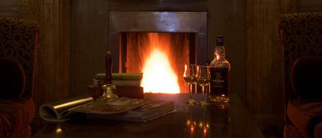 A fireplace with a lit fire, a bottle of liquor, and glasses on a table.