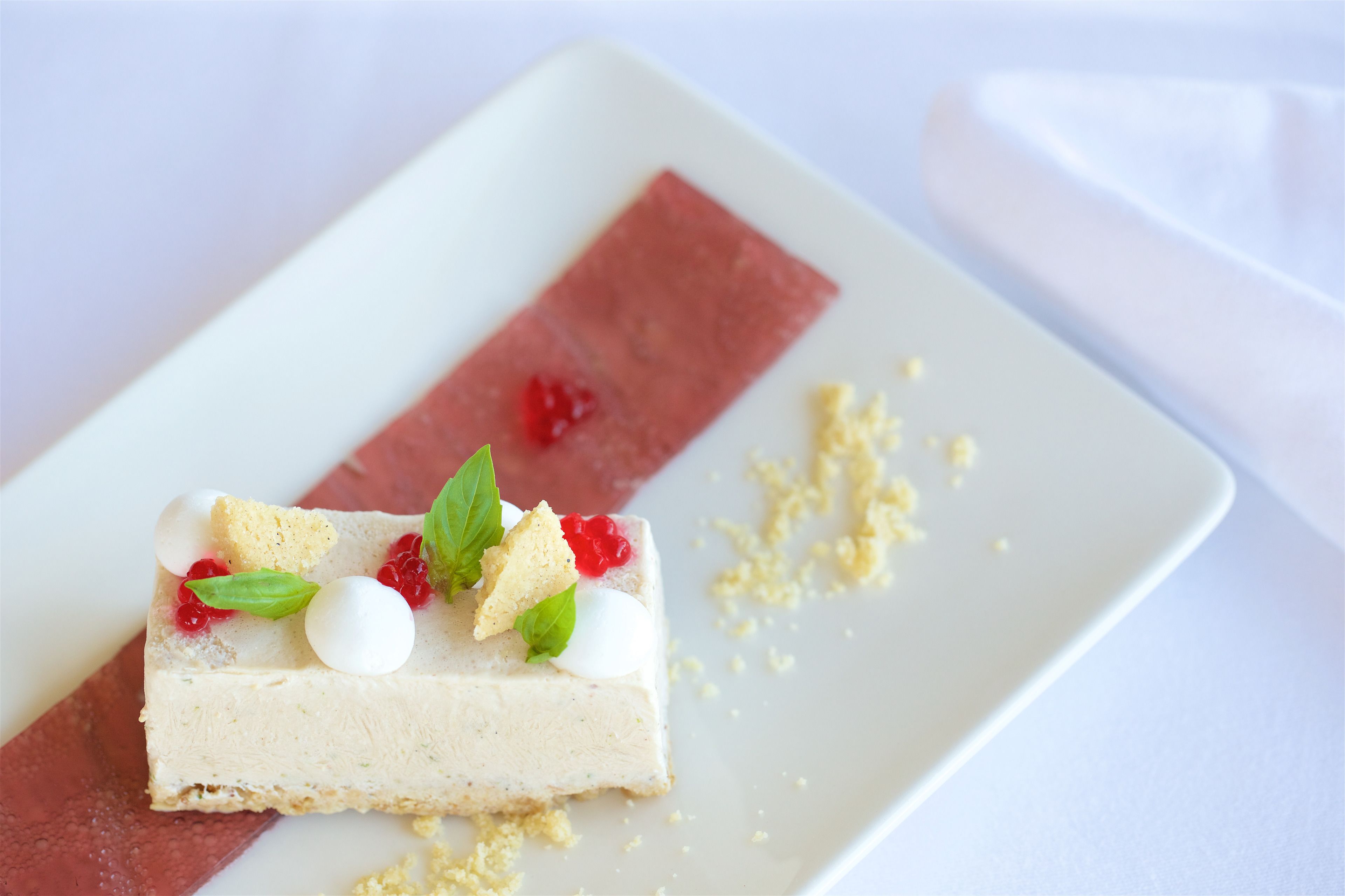 Une part de gâteau au fromage, garnie de fruits rouges et d’une feuille de menthe, présentée sur une assiette blanche.