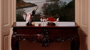 Vista a través de una ventana con una botella de champán, copas y un bol de fresas sobre una mesa de madera.