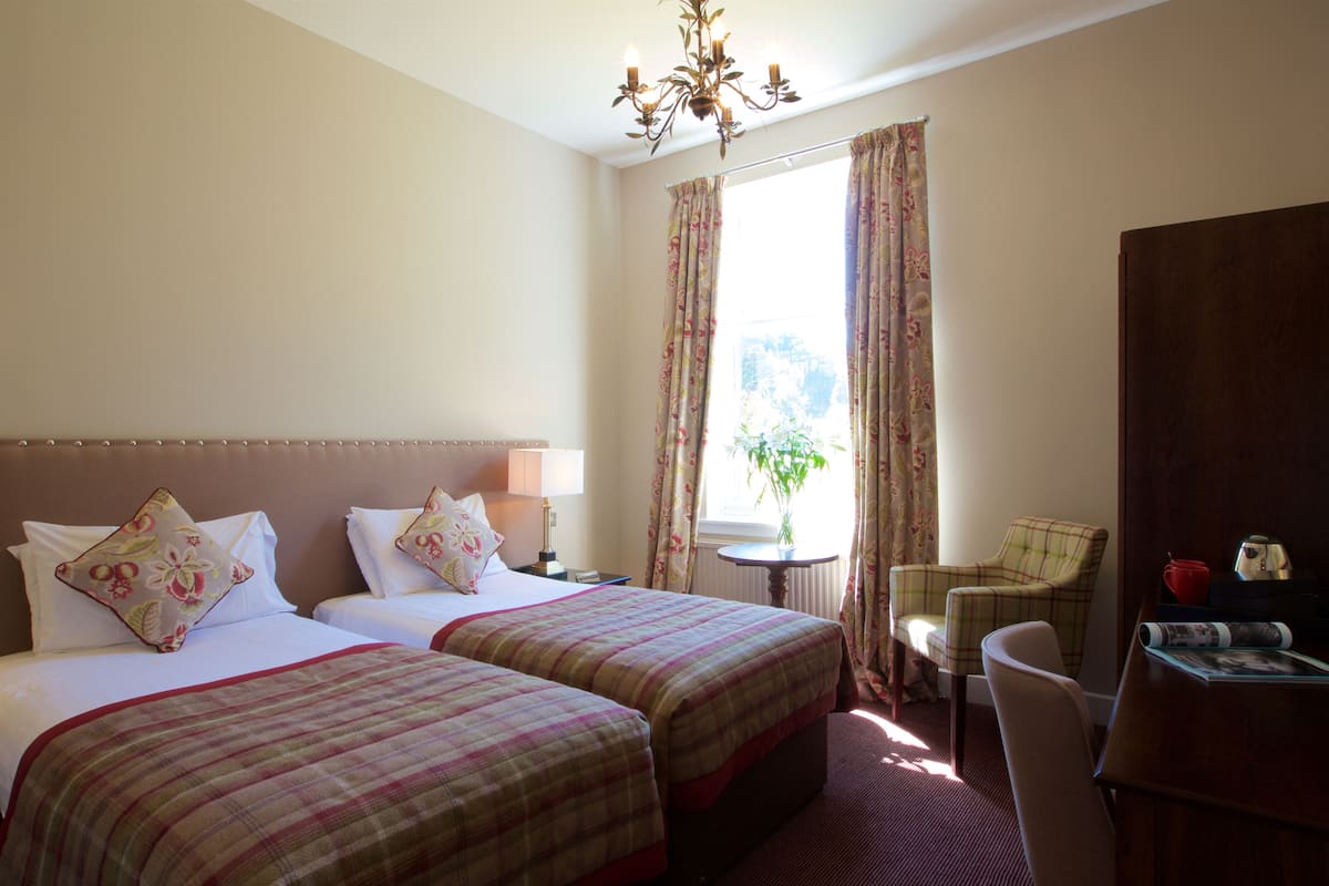 A hotel room with two beds, a desk, a chair, a lamp, and a window with curtains.