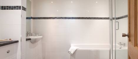 A modern bathroom with a glass shower enclosure, a white bathtub, and a sink with a countertop.