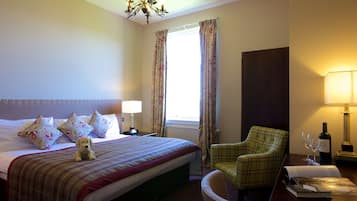 A hotel room with a bed, a chair, a lamp, a bottle of wine, and a window with curtains.