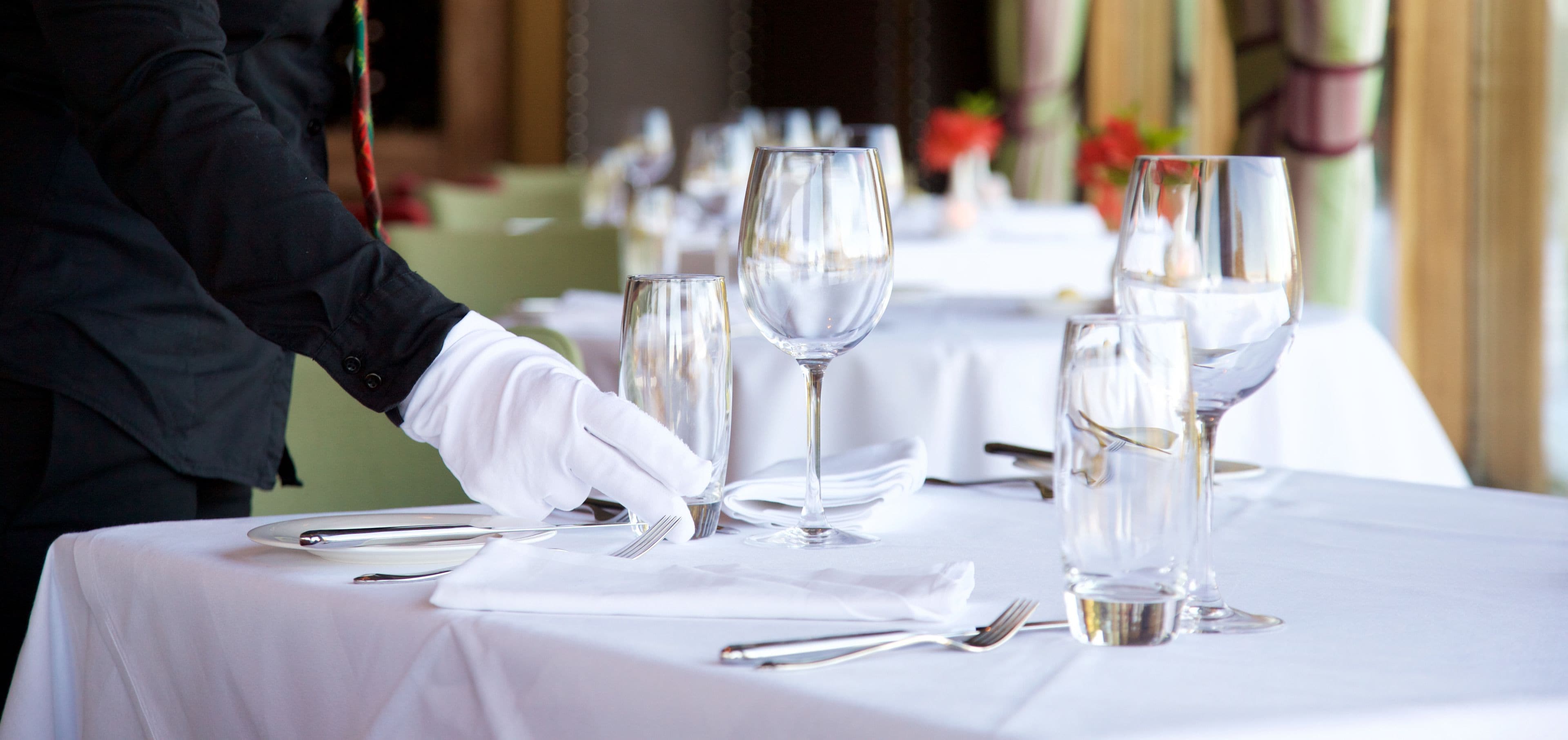 A table set with white tablecloths, silverware, and clear wine glasses.