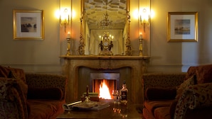 Una habitación con chimenea, dos sofás, una mesa con un libro y vasos, y cuadros en las paredes.