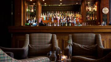 A bar area with a variety of liquor bottles, two plaid armchairs, and a small table with a candle and glasses.