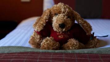 Een bed met een teddybeer, gekleed in een rood shirt met de tekst 'Castle Hotel'.