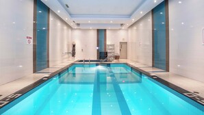 Ein Schwimmbecken mit einem Sprungverbotsschild, gefliesten Wänden und einer zentralen Treppe.