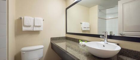 A bathroom with a white toilet, a granite countertop, a white sink, and a large mirror.