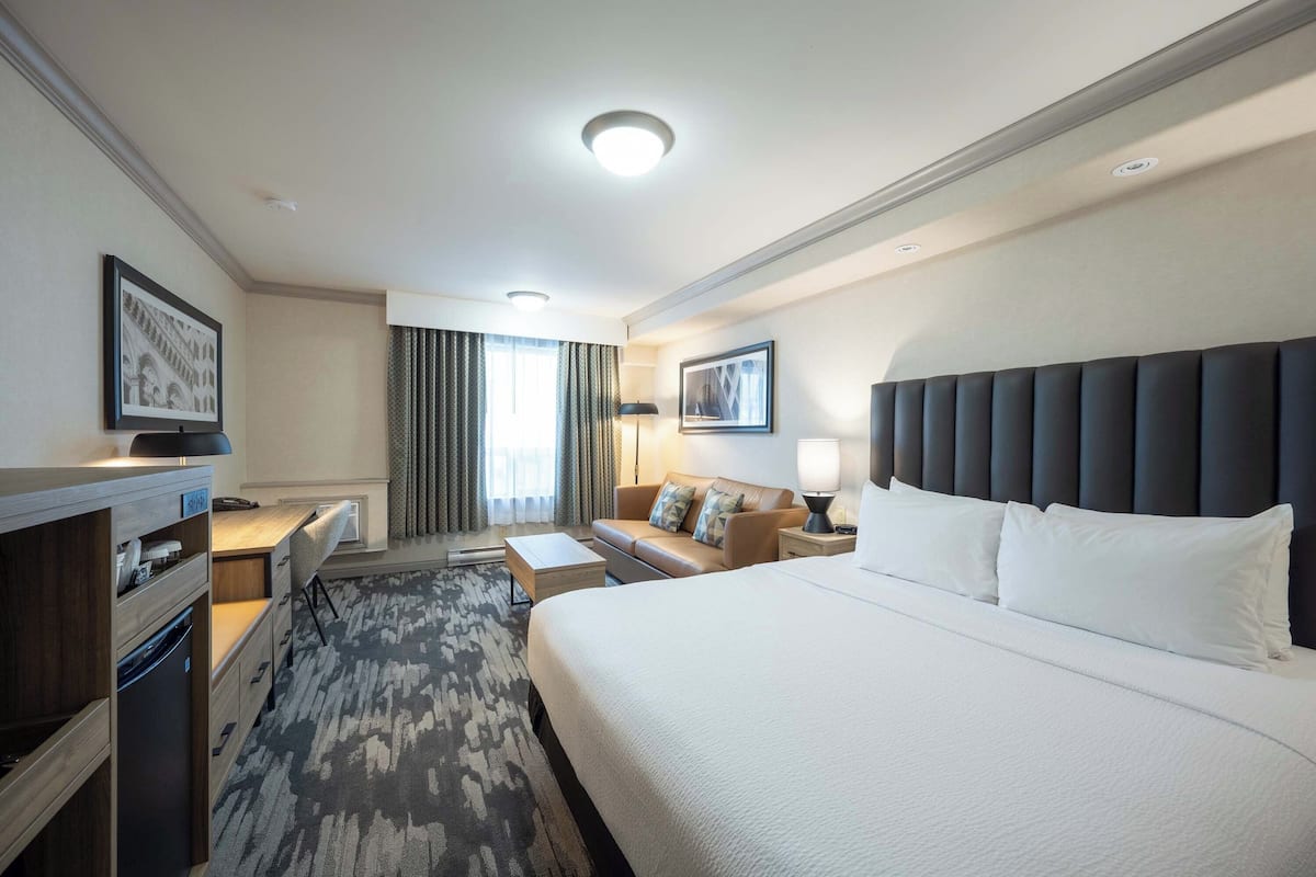 Une chambre d’hôtel avec un grand lit, un bureau avec une chaise, un canapé, une télévision et une fenêtre avec des rideaux.