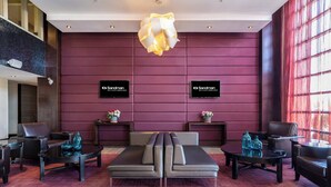 Eine moderne Lobby mit einer zentralen Couch, zwei Beistelltischen mit dekorativen Vasen und einer großen Chandelier.